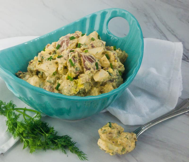 Side view of Best Potato Salad with Bacon in a blue bowl with a spoon of potato salad next to it.